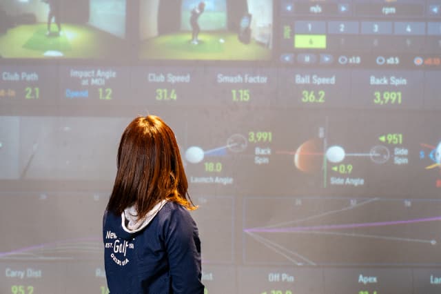 シミュレーションゴルフのショット分析画面を女性が見ている様子