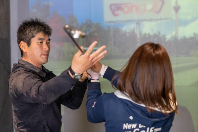 プロによるゴルフレッスンを女性がうけている様子