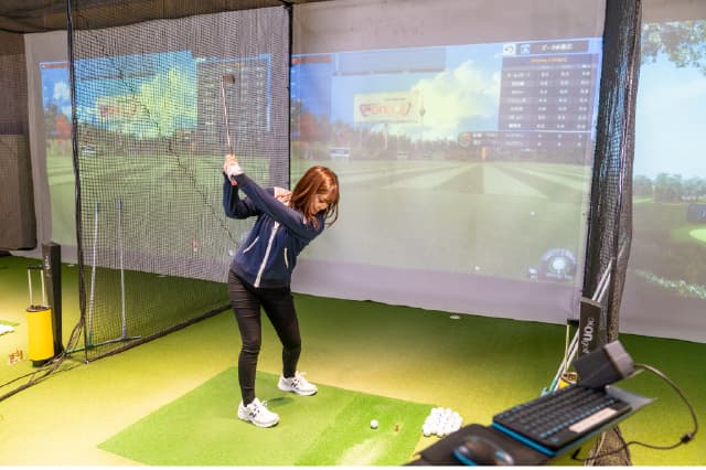 シミュレーションゴルフ打席でスイングしている女性の様子